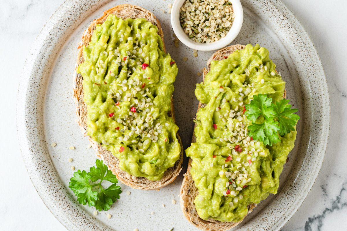 Toast with mashed avocado and hemp seeds on a plate. Healthy vegan snack. Top view, marble background