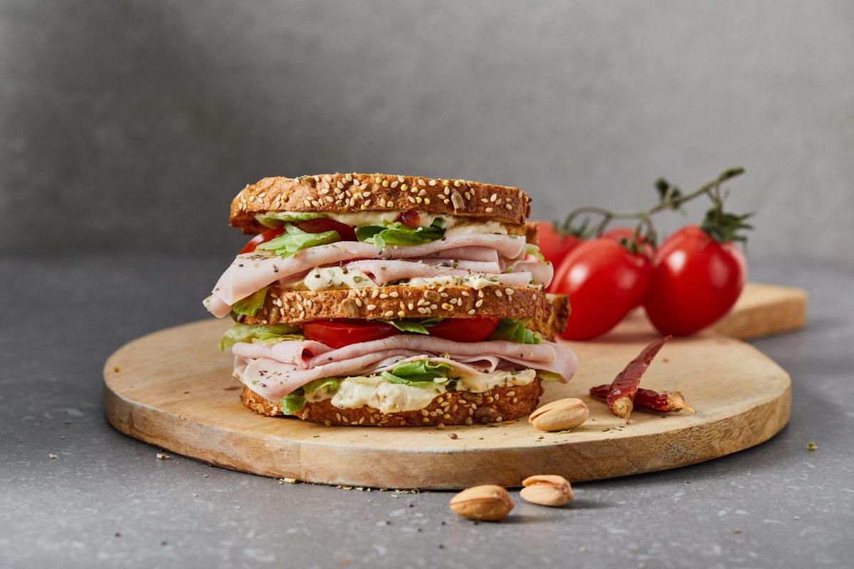 Healthy and tasty protein double sandwich for breakfast, with ham, green salad, cherry tomato and mayo, with fresh herbs, spices  and seasoning, served on a wooden cutting board, on home, bar or restaurant table, representing a healthy lifestyle and wellbeing, a close up hero image with a copy space