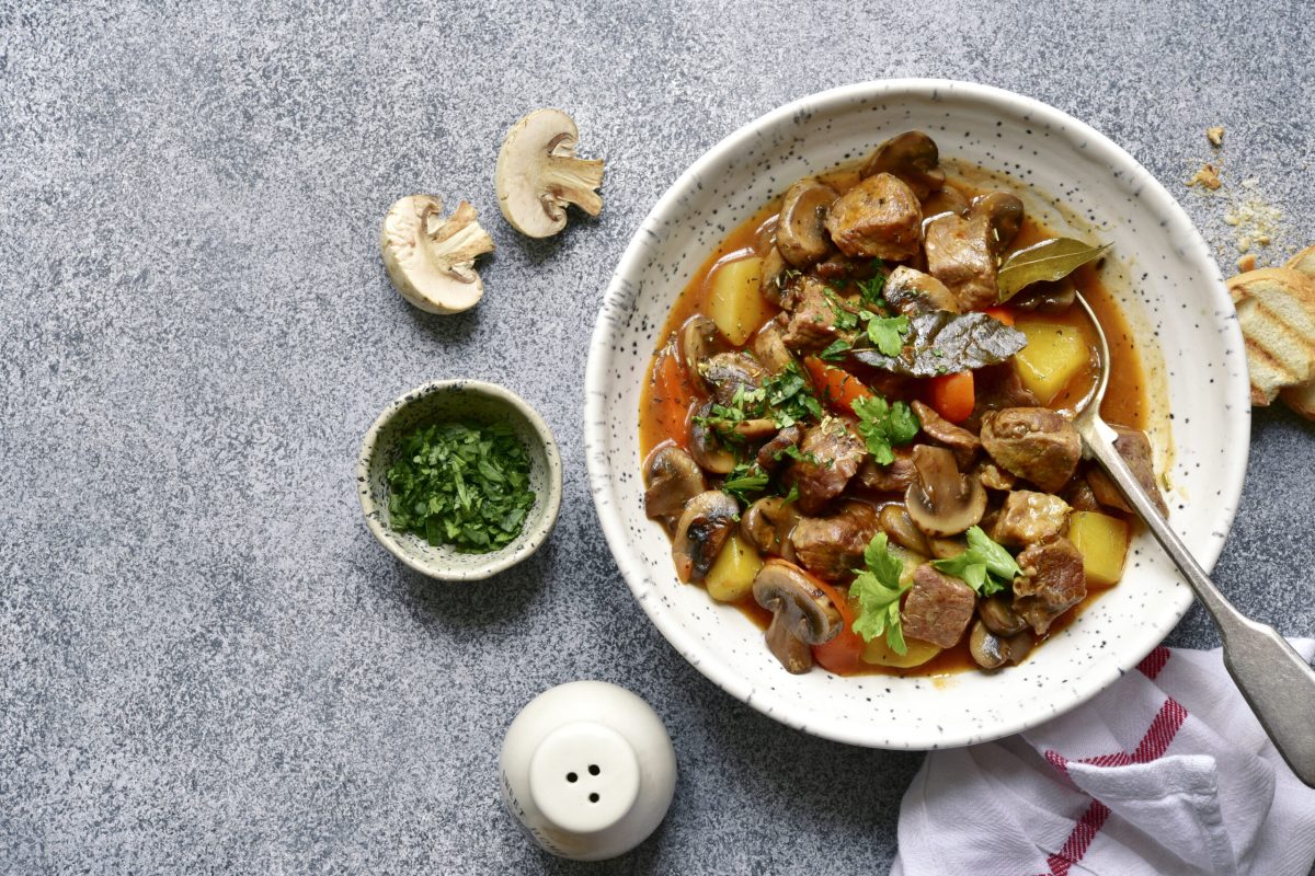 Meat stew ( beef bourguignon ) with vegetable and mushrooms in a white bowl over grey slate, stone or concrete background. Top view with copy space.